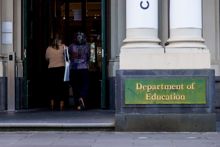 Two woman are shown from behind walking into the Department of Education building.