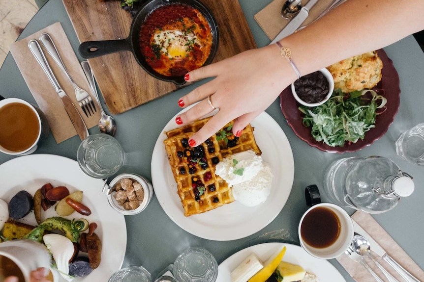 A woman reaches across table laden with food.