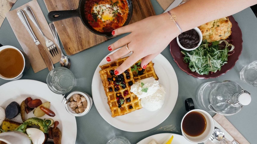 A woman reaches across table laden with food.