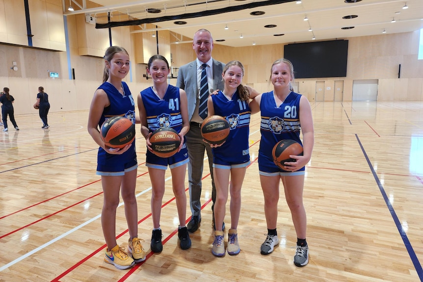 A group of girls with basketballs smiling, with their principal standing behind the group.