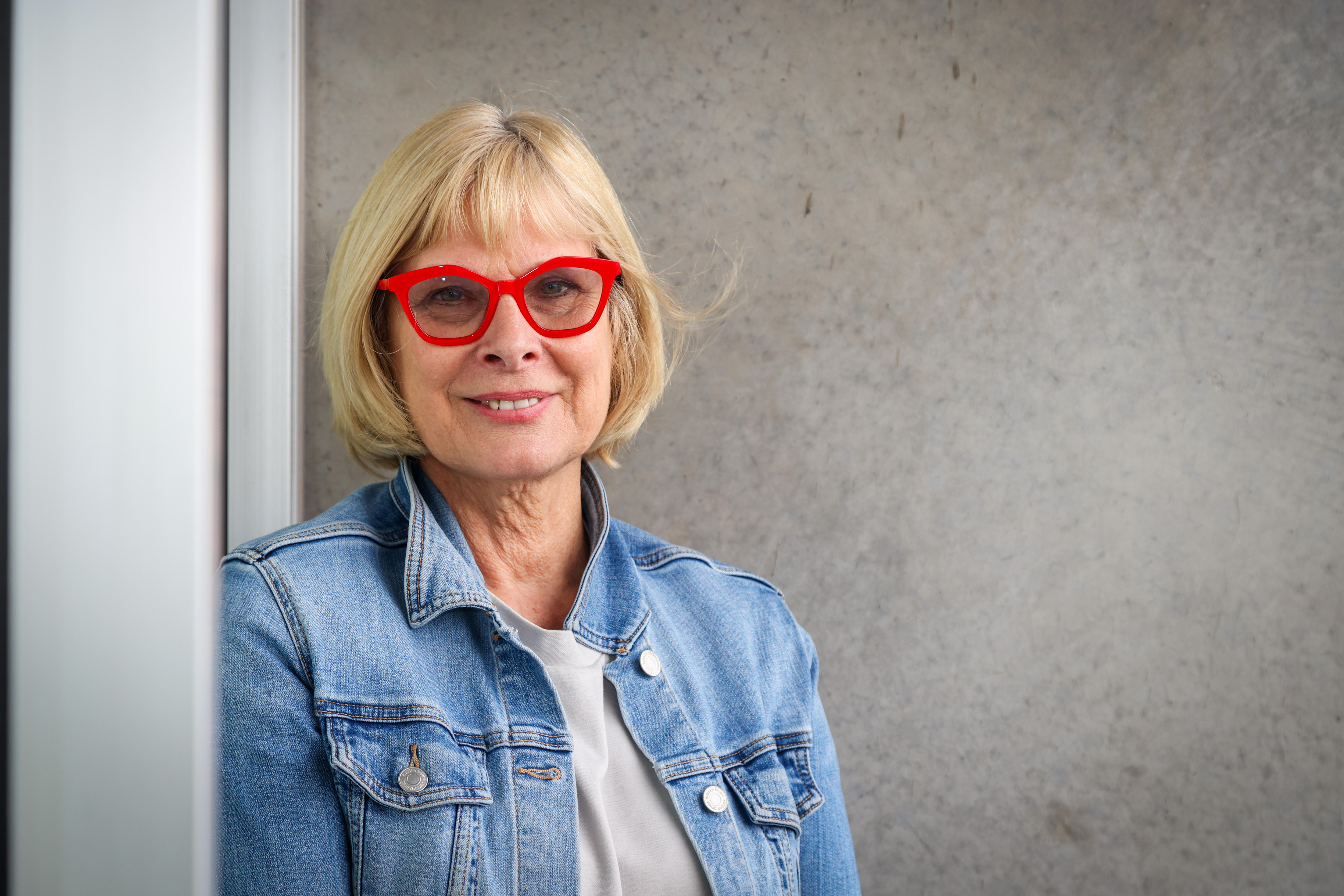 A woman wearing a blue denim jacket and red glasses.
