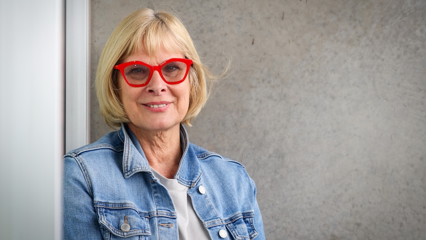 A woman wearing a blue denim jacket and red glasses.