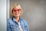A woman wearing a blue denim jacket and red glasses.