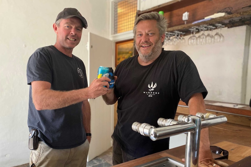 Two men stand behind a bar and cheers