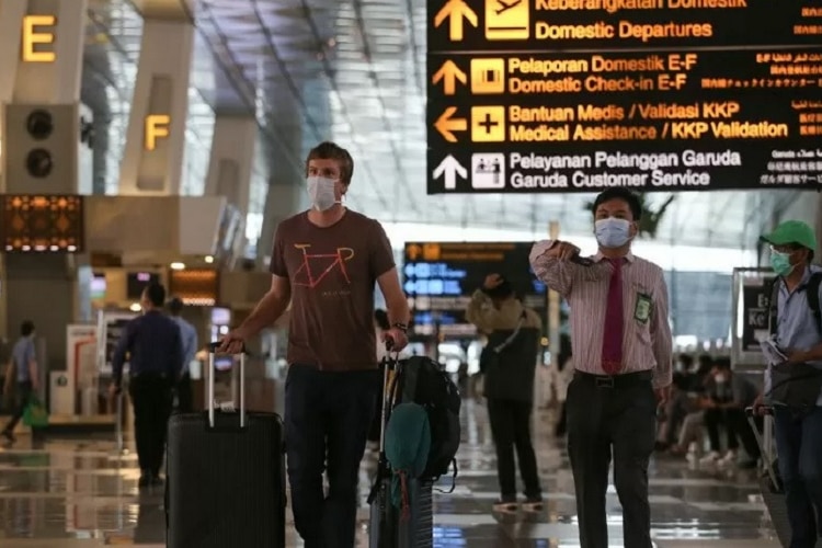 A man wearing mask carrying baggage next to an Indonesian security guard at Jakarta airport.