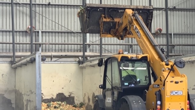 An excavator picks up a pile of food waste in its trough.