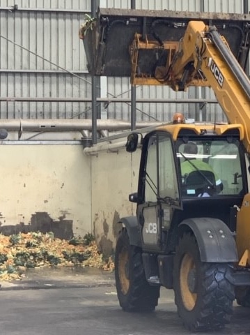 An excavator picks up a pile of food waste in its trough.