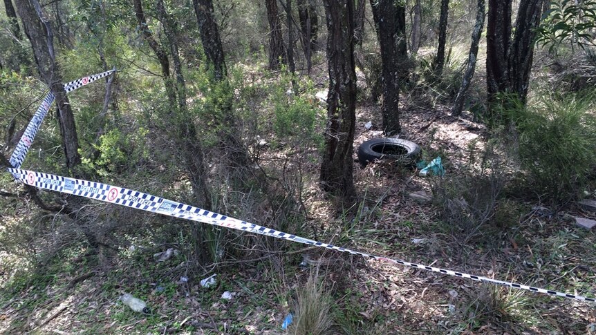 An abandoned car tyre and rubbish surrounded by police tape in bushland