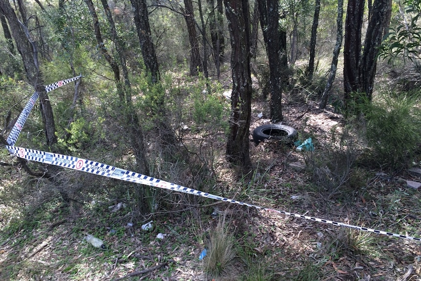 An abandoned car tyre and rubbish surrounded by police tape in bushland.