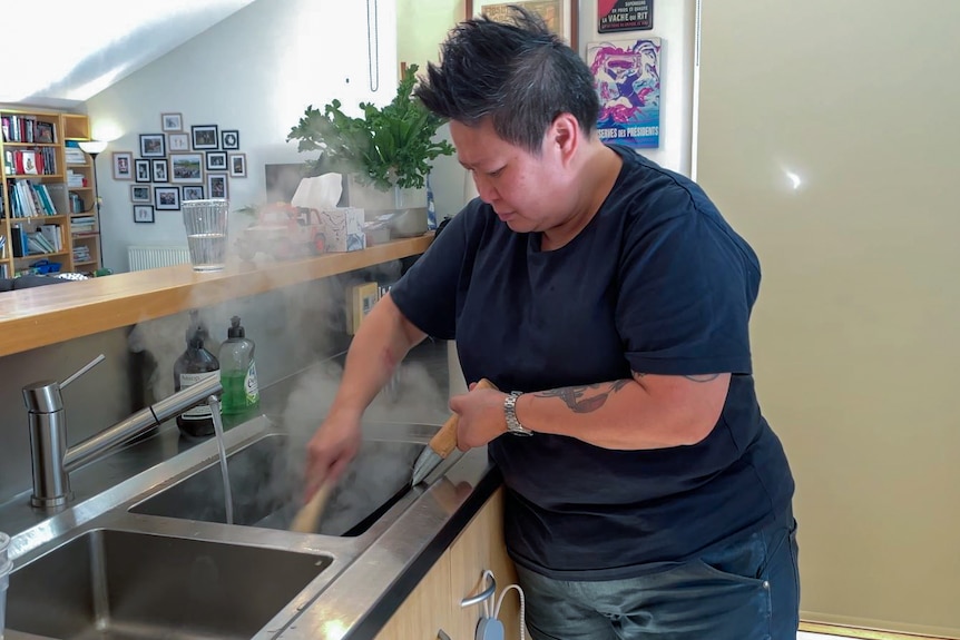 Chef Jerry Mai washes the wok using warm water and a wok brush. Steam rises. from the sink