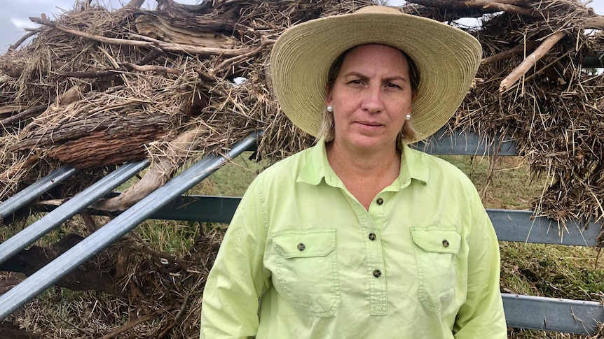 Women with green work shirt on stands in front of cattle yards with debris all over it