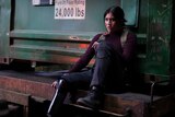 A TV still of Alaqua Cox, a Native American actor in her mid-20s, looking tough. She is wearing a backpack and large boots.