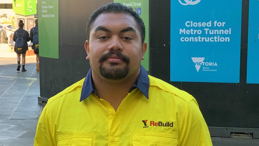 A man wearing a bright yellow work shirts stands near a  Metro Tunnel construction site.