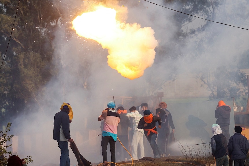 A small fireball and smoke fills the air as a group of farmers clash with police.