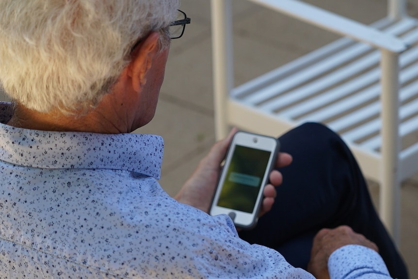 Man with white hair holds a mobile phone.