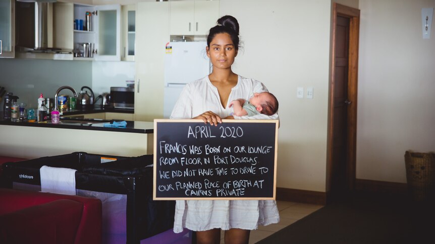 woman holding baby and sign in lounge room