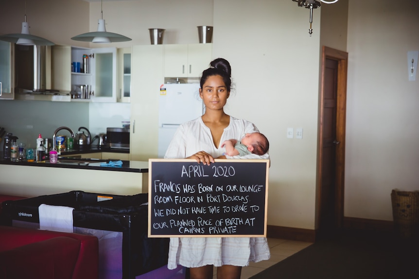 woman holding baby and sign in lounge room