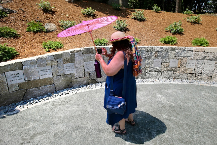 A woman with a parasol stands in front of a memorial wall