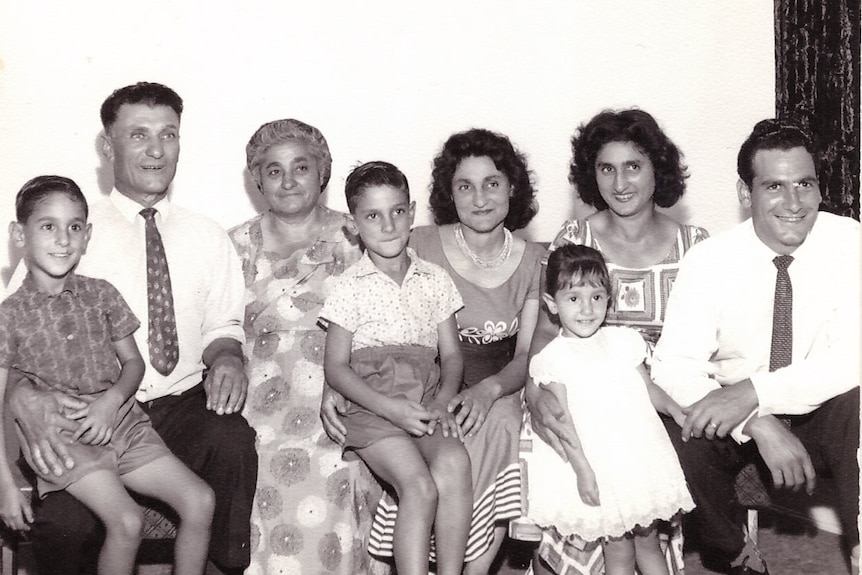 Grandparents, aunty and parents sit with three children in a black and white photo. 