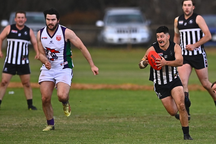 A man wearing a black and white football jumper runs while holding a red football. 