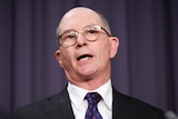 Kelly, a bald man with glasses, is mid-speech.