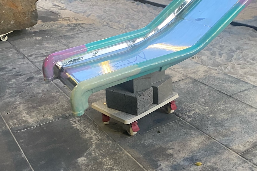 A photo of a metal slide with the end sitting on bricks on a platform with wheels