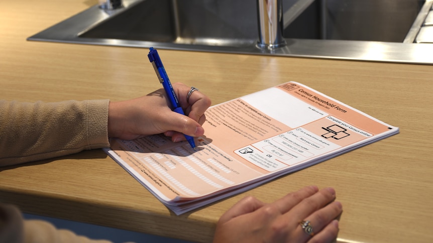 A hand holds a pen to an orange Australian census form.