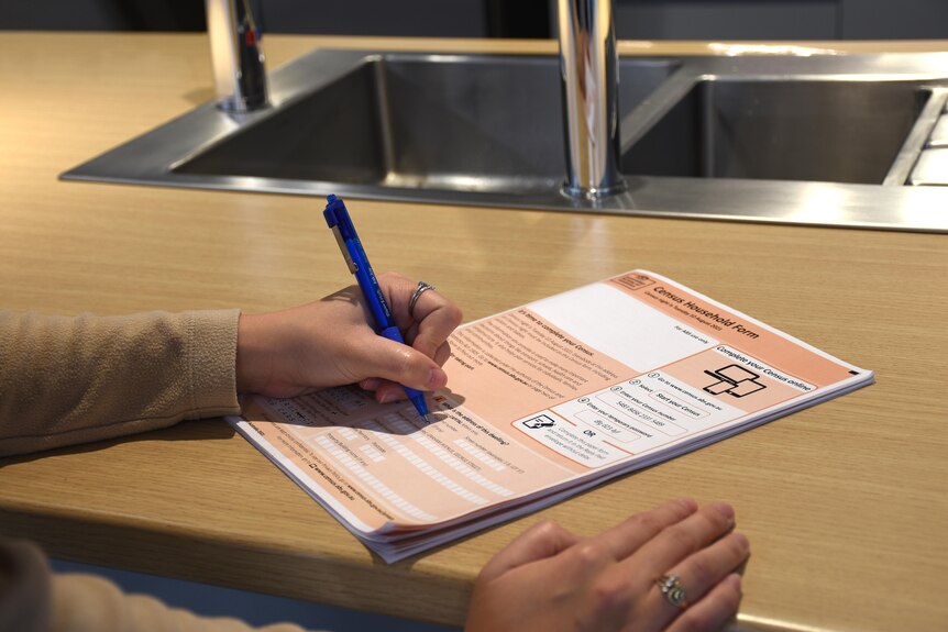 A hand holds a pen to an orange Australian census form.
