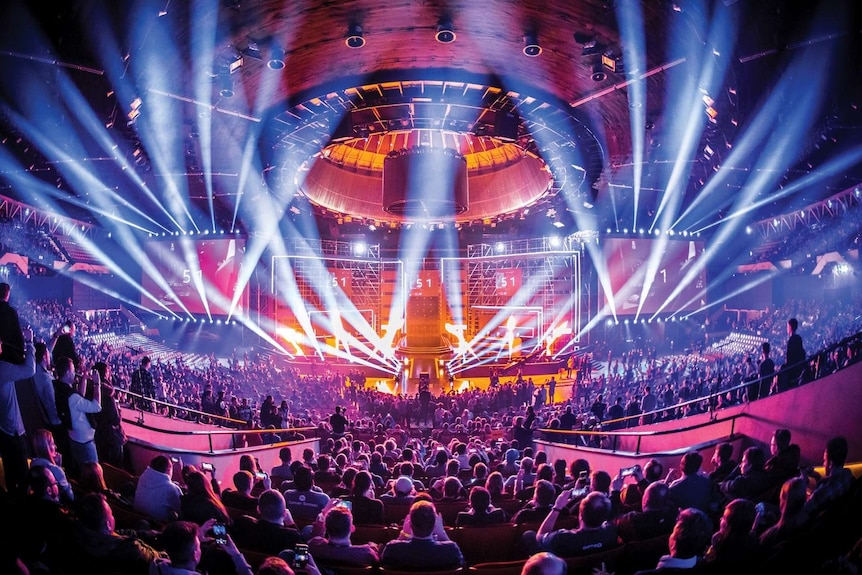 A wide shot of a packed esports arena with lights strobing from the ceiling.