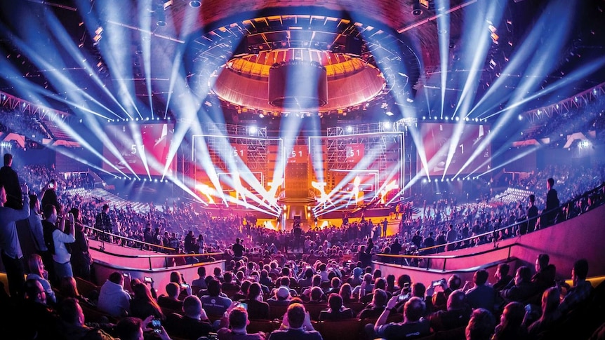 A wide shot of a packed esports arena with lights strobing from the ceiling.