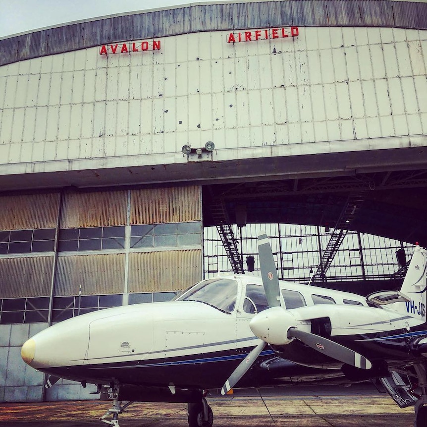 A private plane parked outside a hangar, with the words Avalon Airport at the top of the hangar.