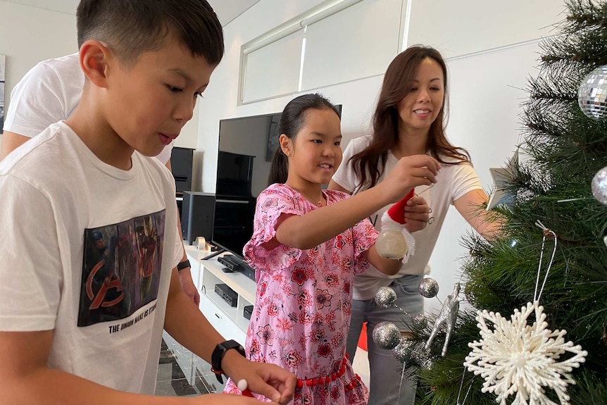 A family of four put decorations on a Christmas tree in their living room.