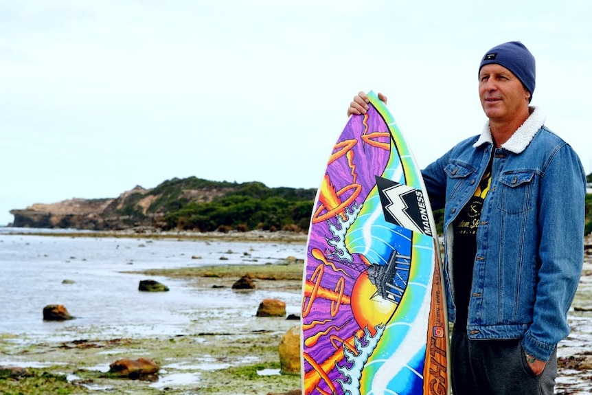 Jeremy Ievins with one of his painted surfboards on the shore at Port Macdonnell