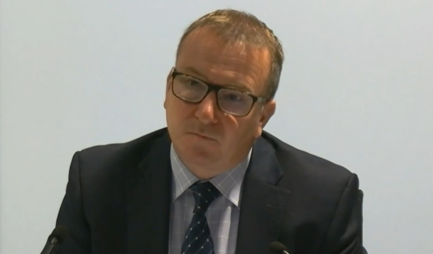 A man dressed in a suit and a tie, wearing glasses.