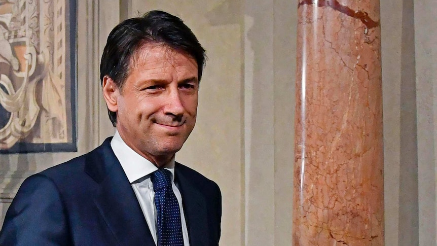 Giuseppe Conte smiles next to a large pillar