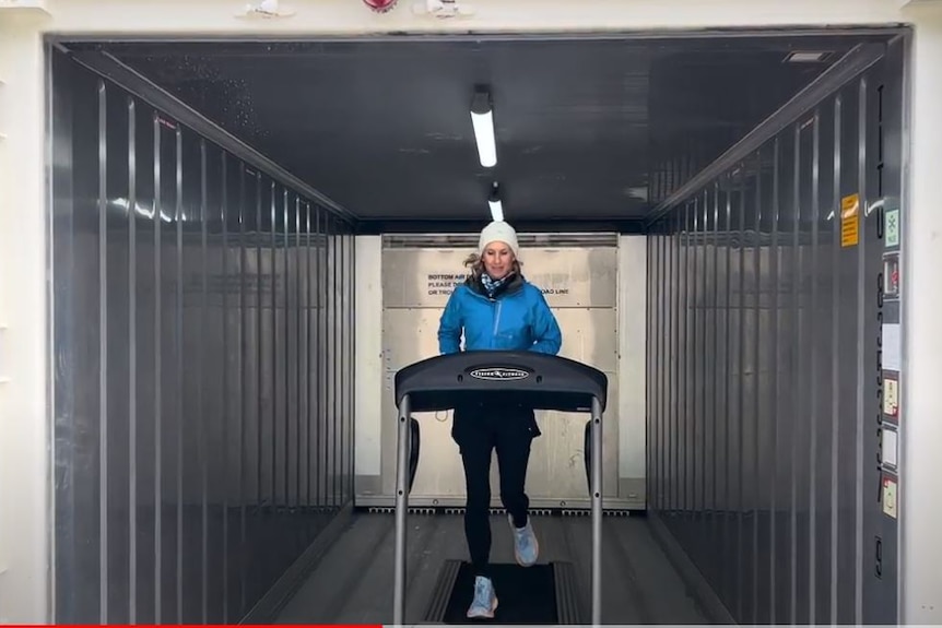 Woman in winter gear and beanie running in a shipping container-sized freezer