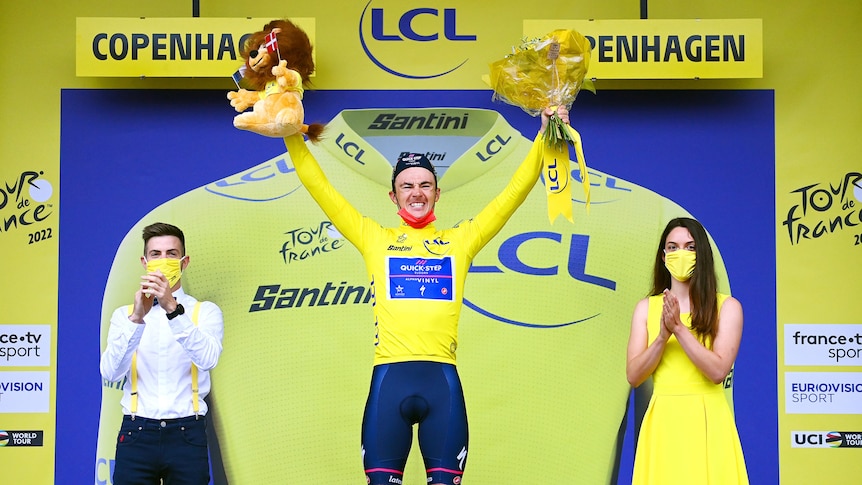 A man in a yellow jersey holds some flowers and a lion in the air with a yellow and blue background
