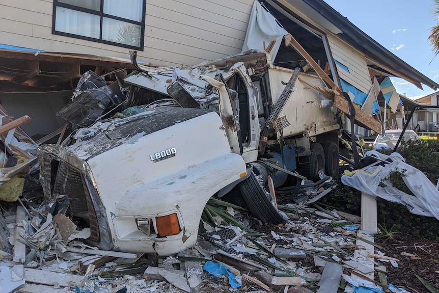 A two-storey white house with a grey roof destroyed by the impact of a truck crash.