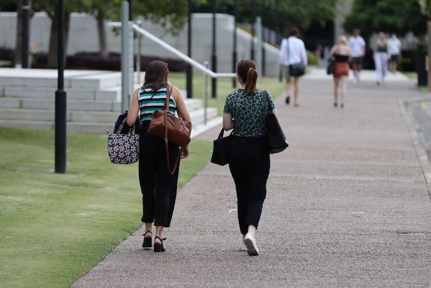 two female students carrying handbags walk through a university campus. they are facing away from the camera