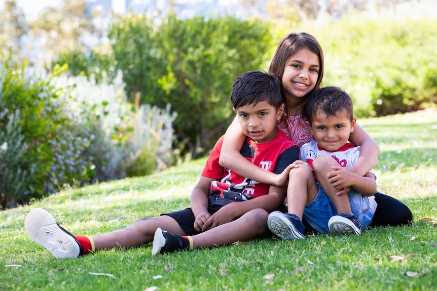 Three children sitting together on grass.