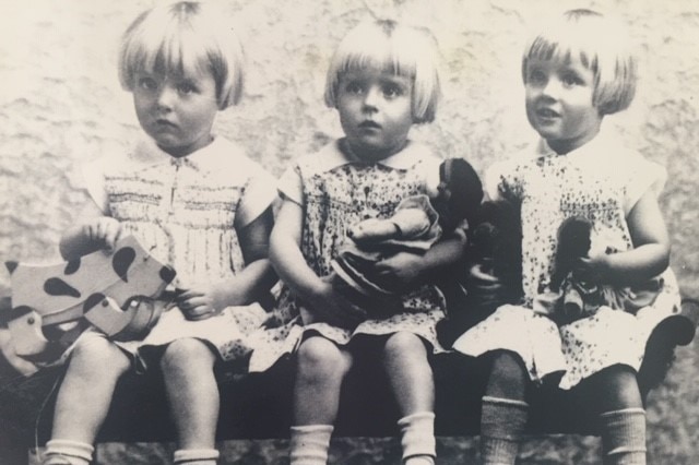 An old black-and-white photograph of three blonde toddlers holding toys.