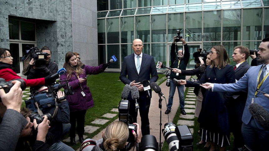 A wide shot showing Peter Dutton speaking to many journalists and cameramen outside Parliament