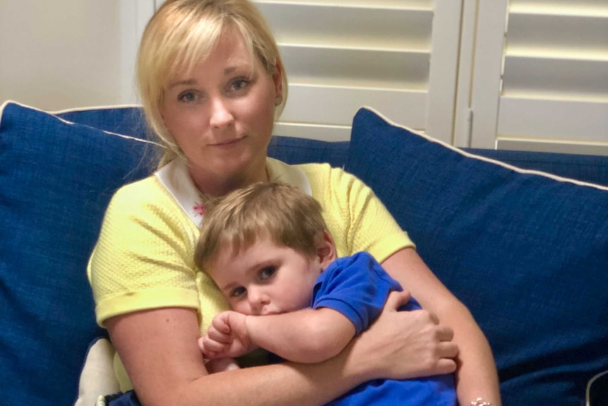 A mother hugs her son on a couch at home.