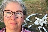 A selfie of a woman in front of a pile of animal bones on the ground, for a story about volunteering at National Park.