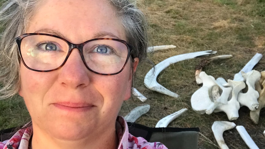 A selfie of a woman in front of a pile of animal bones on the ground, for a story about volunteering at National Park.