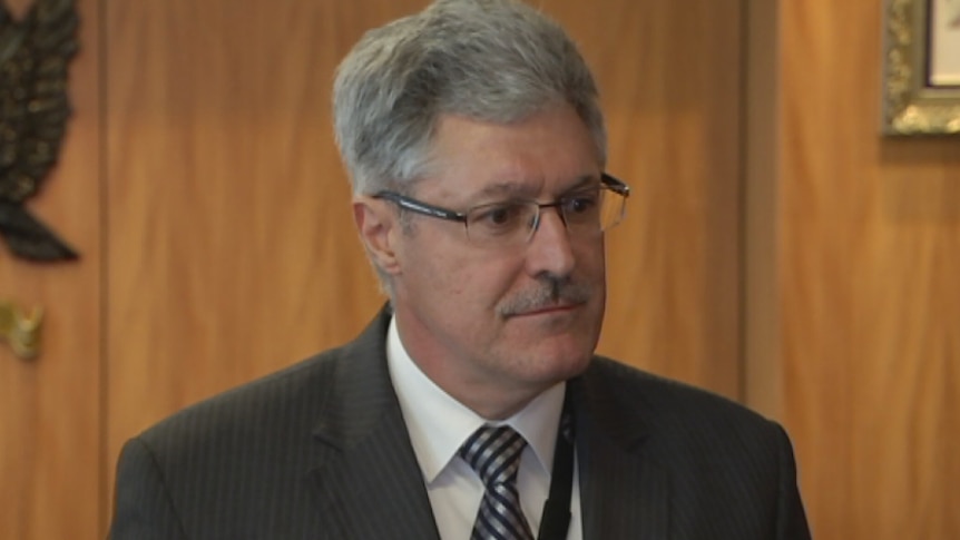 A head and shoulders shot of a man in a suit and tie looking off camera in a conference room.