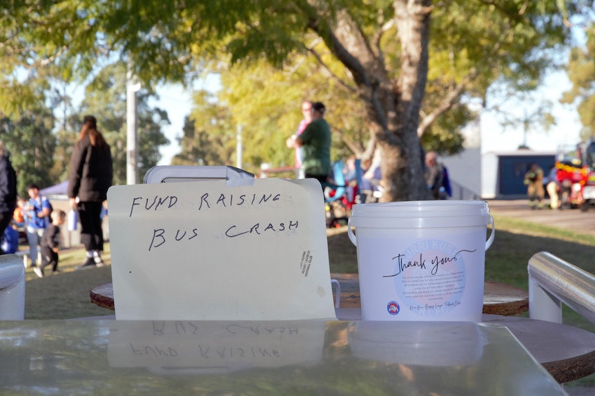 a bucket collecting coin donations sits next to a hand written sign that says "fundraising bus crash"