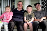 Raeleen sits with her three grandkids - a little girl wearing pink and two boys in T-shirts - out the front of their house.