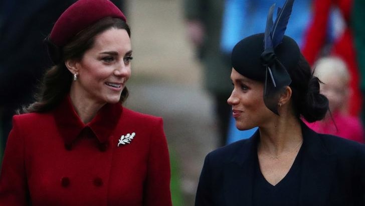 Kate wears a red hat and coat as she walks alongside Meghan, wearing a blue feathered hat and coat.