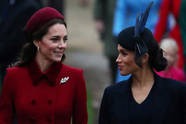 Kate wears a red hat and coat as she walks alongside Meghan, wearing a blue feathered hat and coat.